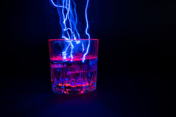 A vessel, a glass filled with a transparent liquid with an electric lightning and beating from the surface. On a black background