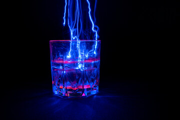 A vessel, a glass filled with a transparent liquid with an electric lightning and beating from the surface. On a black background