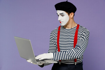 Charismatic amazing marvelous vivid young mime man with white face mask wears striped shirt beret hold use work on laptop pc computer isolated on plain pastel light violet background studio portrait.
