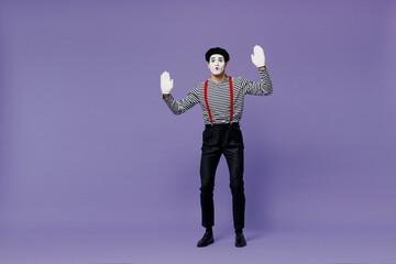 Full size body length young mime man with white face mask wears striped shirt beret stand hands palms raised like touch invisible wall isolated on plain pastel light violet background studio portrait.
