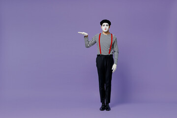 Full size body length young mime man with white face mask wear striped shirt beret hold raised empty palm with copy space place mock up isolated plain pastel light violet background studio portrait