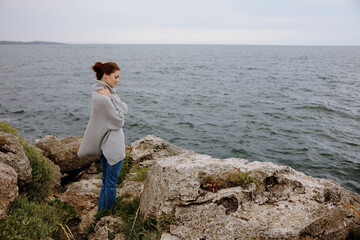 Fototapeta na wymiar pretty woman in a gray sweater stands on a rocky shore nature Lifestyle
