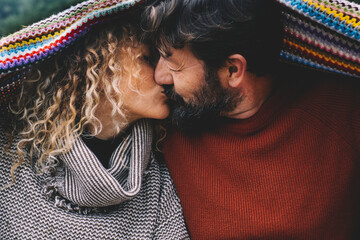 Couple in love kissing under a colorful woolen blanket. Concept of mature people in relationship...