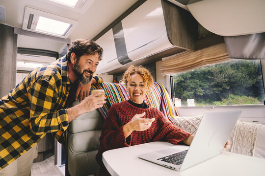 Adult couple enjoy work together using laptop computer sitting inside camper rv vehicle. Concept of nomad and alternative free job lifestyle. Modern man and woman people with technology