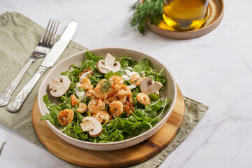 Arugula salad with shrimp and champignons, olive oil and dill on a wooden board on a white surface