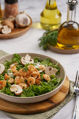 Arugula salad with shrimp and champignons, olive oil and dill on a wooden board on a white surface