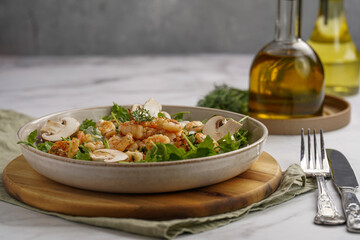 Arugula salad with shrimp and champignons, olive oil and dill on a wooden board on a white surface
