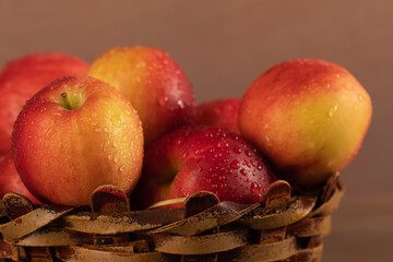 A vase of red apples on a uniform brown background. Wicker basket with seasonal harvest fruits