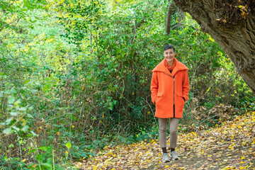 middle-aged woman in orange coat posing in park