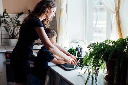 mother and son wash fresh vegetables with water in the kitchen