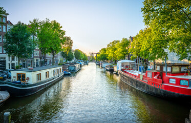 Sch&ouml;ner Sonnenuntergang &uuml;ber Amsterdam Stadt Landschaft in Niederlande mit Blumen und Fluss an der Br&uuml;cke im Sommer. Natur Haus Boot Architektur Gracht