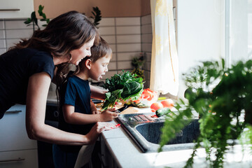 mother and son prepare fresh vegetables for salad at lunch in the kitchen