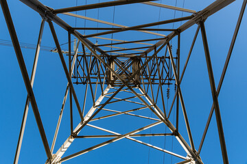 Double-circuit aerial power transmission tower against blue sky. Steel structure with wide base at the bottom. Insulators on supports made of glass, porcelain.