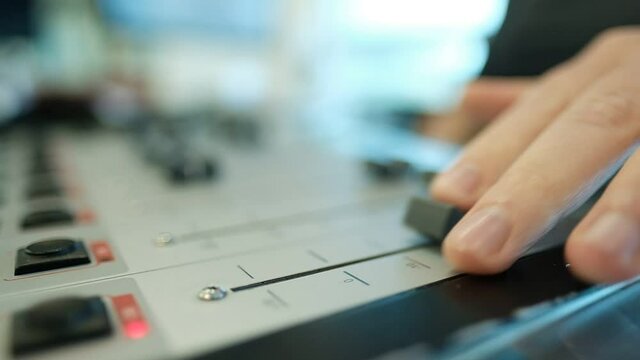 An extreme shallow depth of field on a sound console, close to the camera, where the sound engineer reaches forward to move a slider button, back and forth. radio station, Israel.