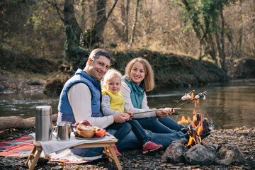 A family fries marshmallows on sticks by the fire.