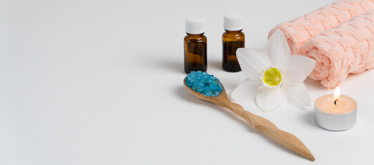 Banner with sea salt in a wooden spoon, candle, aromatic oil in bottles, towels and a flower on a white background. Relaxation and massage in the spa salon. Body care concept.