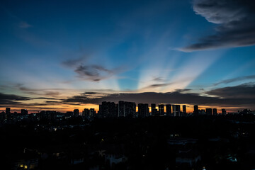 Colourful sunset with rays of sun and silhouette of city skyline and clouds