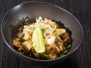 wok, fried chicken fillet slices with noodle, bamboo shoots, parsley and nuts in a bowl on dark background