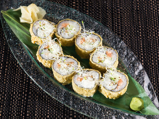 hot sushi roll with salmon and avocado breading on a glass plate, close up photo on dark background