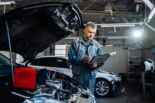 Car service, repair, maintenance concept. Caucasian man car mechanic using a computer laptop to diagnosing and checking up on car engines parts for fixing and repair.