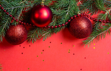 Red background with Christmas decorations from fir branches and Christmas balls. Bright red Christmas and New Year background, Free space for your text. Natural spruce branches.