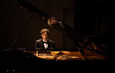 Young 20s aspiring musician playing grand piano on a stage of a huge concert hall © supamotion