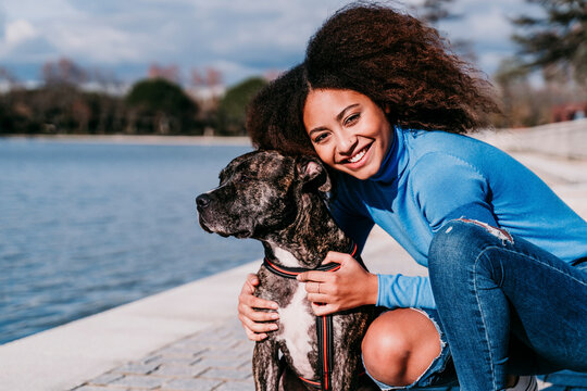 Smiling curly hair woman crouching by dog on sunny day