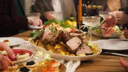 Friends celebrating new year, sitting at dining table. Eating roasted meat for main course. Young people students during christmas party at home, drinking champagne, toasting close-up.