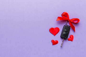 Car key with a red bow and a heart on Colored table. Giving present or gift for valentine day or...