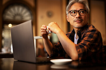 Businessman working on laptop in cafe. Handsome senior man enjoying in fresh coffee..