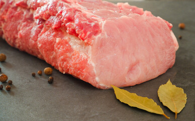 Raw meat. Uncooked fresh pork. A large juicy fresh piece of meat on a gray stone during cooking. Pepper, bay leaf. Culinary concept.