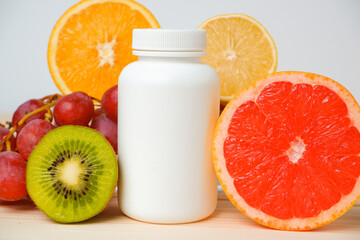 Vitamins. White container for vitamins on a background of fruits. Citrus, lemon, orange, grapes. Blank Medicine bottle