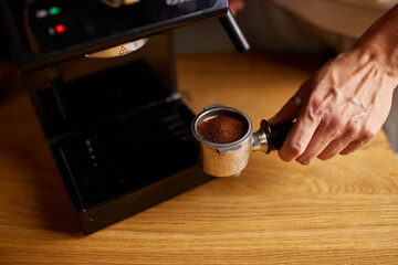 Fototapeta na wymiar Female hands holding portafilter and making fresh aromatic coffee at home using a modern coffee maker, Male barista hand making espresso from ground coffee maker at modern cafe.