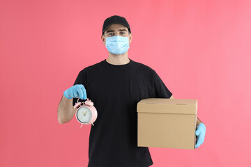 Delivery man holds alarm clock and bag on pink background