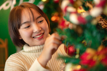 Happy beautiful woman in sweater is smiling to holding glittering balls and decoration to decorate on christmas tree