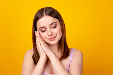 Photo of young pretty lady arms touch cheeks sleepy dreamy relax isolated over yellow color background