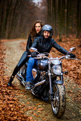 Couple of motorcyclists with a chopper in the woods in the fall.