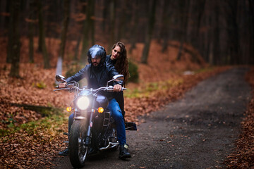 Couple of motorcyclists with a chopper in the woods in the fall.