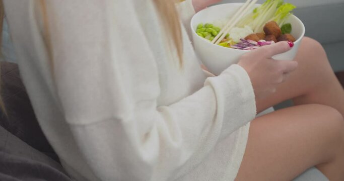 Female wearing erotic lingerie and casual jumper sits on couch holding fresh vegan salad bowl