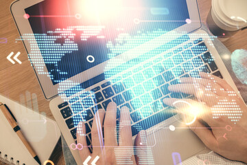 Multi exposure of man's hands typing over computer keyboard and world map hologram drawing. Top view. Technology concept.