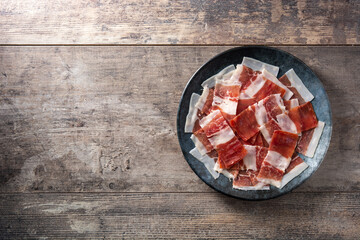 Spanish serrano ham slices on black plate on wooden table. Copy space
