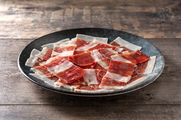 Spanish serrano ham slices on black plate on wooden table