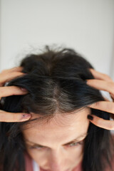 Fototapeta premium Portrait of a beautiful young woman examining her scalp and hair in front of the mirror,