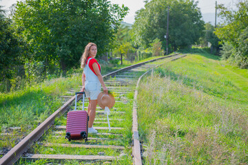 blonde girl with hat walking on the railroad with a suitcase