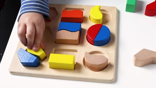 Educational toys, Cognitive skills, Montessori activity. Closeup: Hands of a little Montessori kid learning about color, shape, sorting, arranging by engaged colorful wooden sensorial blocks. 
