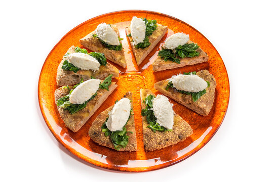 Venetian creamed cod quenelle with spinach on slices of wholemeal focaccia bread, on orange plate isolated on white