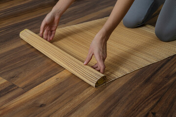 Woman rolling yoga mat made of natural straw.Relaxible practices indoors