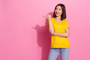 Photo of pretty shiny young lady dressed yellow clothes smiling looking pointing thumb empty space isolated pink color background