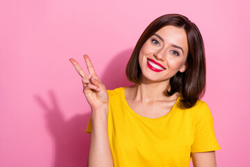 Photo of shiny pretty young lady dressed yellow clothes smiling showing v-sign isolated pink color background