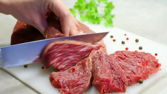Cutting meat fillets. A damask steel knife with a pattern cuts red meat. Chopped beef, slices, abolition of vegetarianism, semi-finished meat products, soy meat. Garnish with parsley and allspice